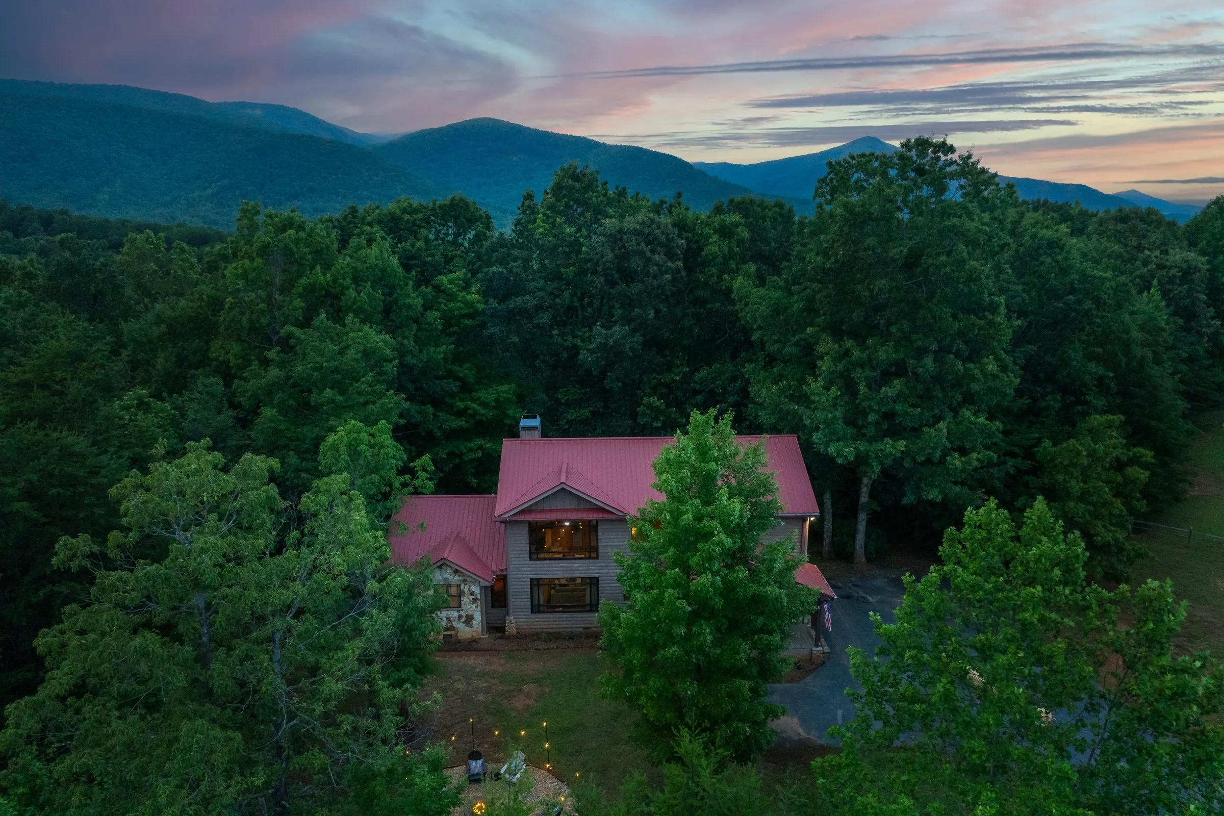 Aerial view of the cabin among trees at dusk with mountains beyond