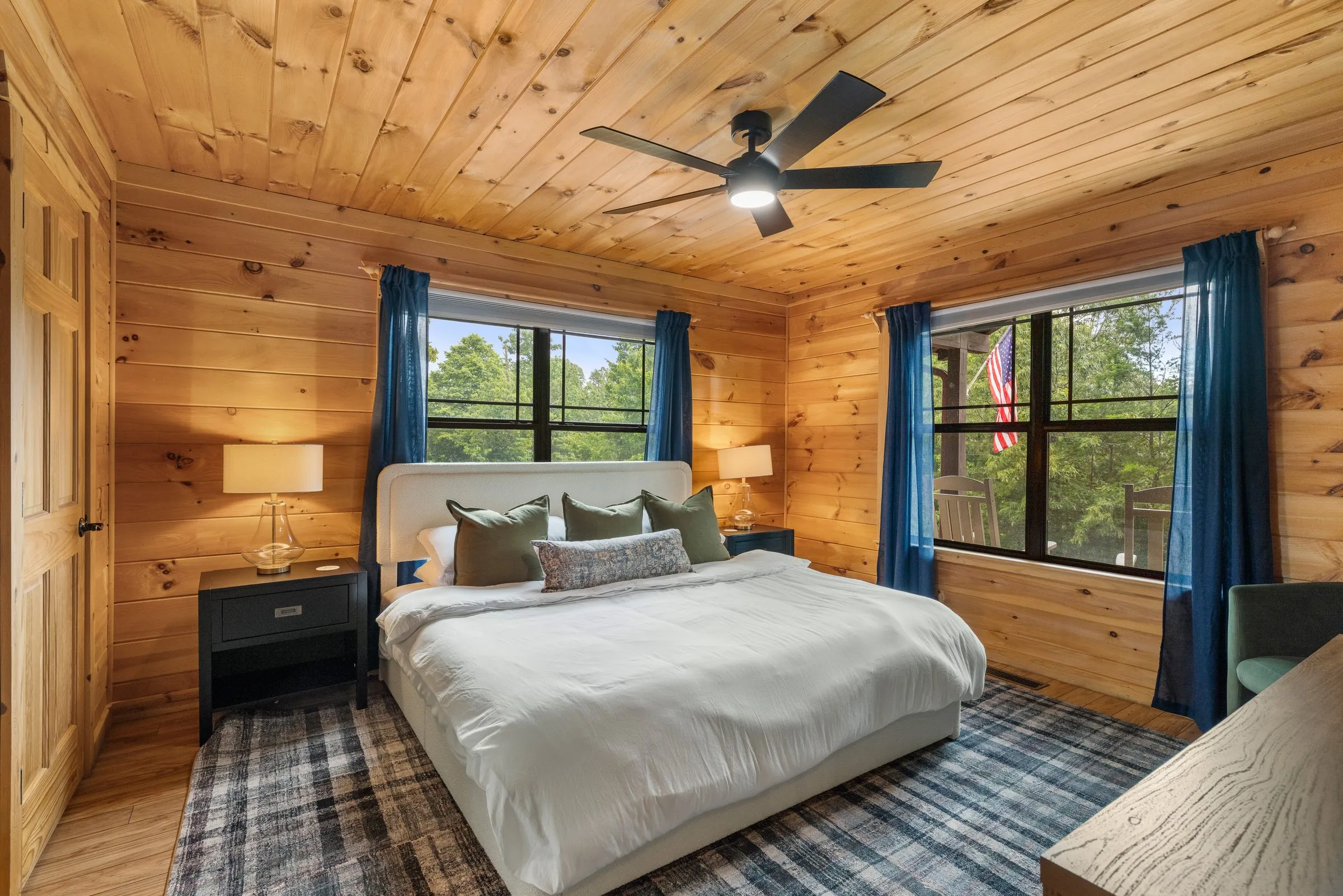 Bedroom 2 seen from the doorway: a king bed with an upholstered headboard, blue curtains and windows onto the trees